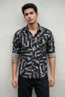 Man wearing a cotton dobby floral printed casual shirt in charcoal black with large-scale olive and cream abstract print, spread collar, contrast cuff lining, chest patch pocket with logo badge, and full sleeves rolled at the cuffs