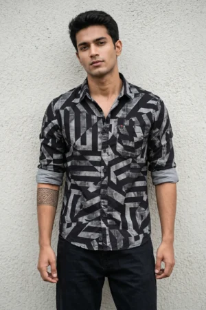 Man wearing a cotton dobby floral printed casual shirt in charcoal black with large-scale olive and cream abstract print, spread collar, contrast cuff lining, chest patch pocket with logo badge, and full sleeves rolled at the cuffs